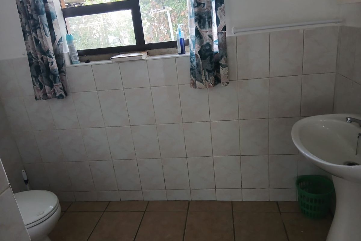 A functional bathroom featuring a pedestal basin, toilet, and tiled finishes throughout, offering a clean and practical space.