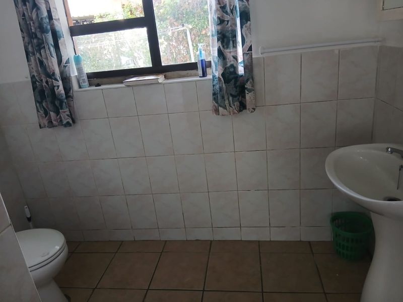 A functional bathroom featuring a pedestal basin, toilet, and tiled finishes throughout, offering a clean and practical space.