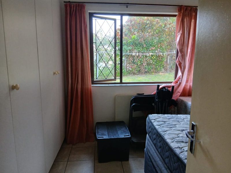 A bedroom featuring built-in cupboards, tiled flooring, and a window with a security gate overlooking the rear garden.