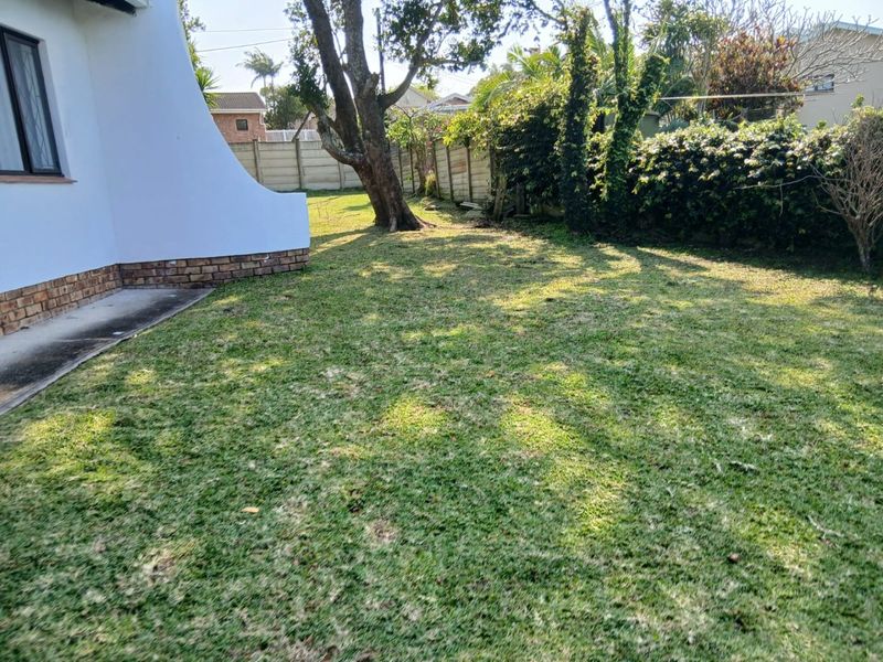 A view of the rear garden featuring a lawn area, mature trees, and a precast concrete boundary wall.