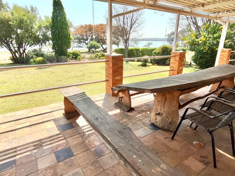 A covered outdoor patio featuring brick pillars, metal railings, and tiled flooring, overlooking a spacious garden with scenic views.