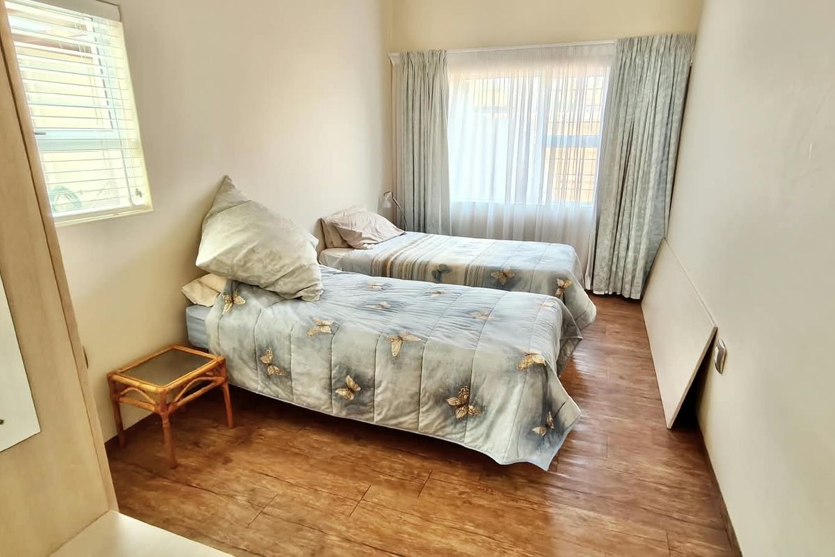 A functional bedroom featuring laminate flooring, a built-in cupboard, and large windows with curtain tracks, providing ample natural light.