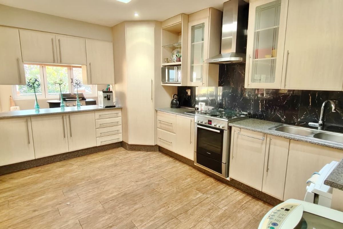 A functional kitchen featuring light-toned cabinetry, a dark tiled splashback, stainless steel appliances, and wood-look flooring.
