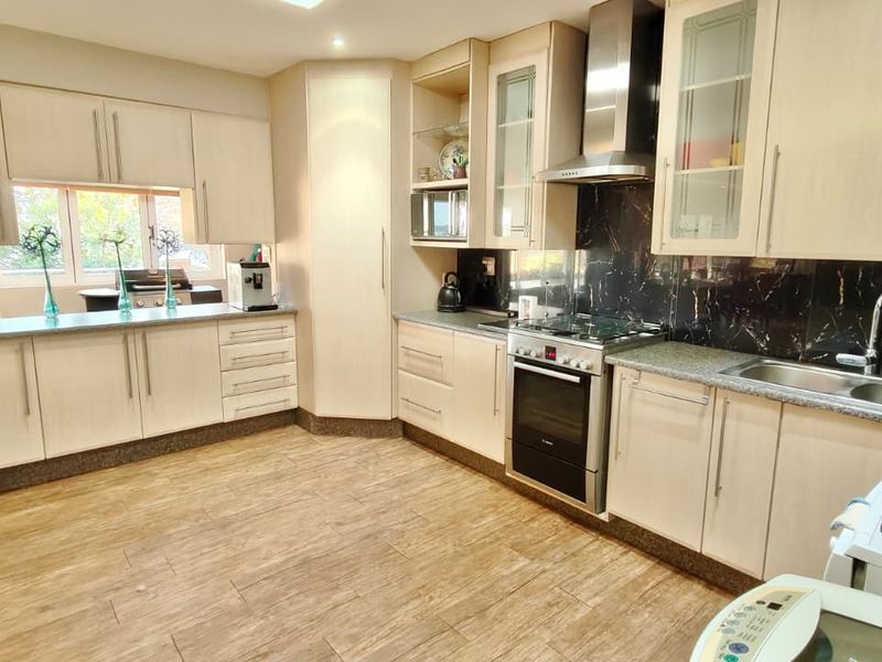 A functional kitchen featuring light-toned cabinetry, a dark tiled splashback, stainless steel appliances, and wood-look flooring.