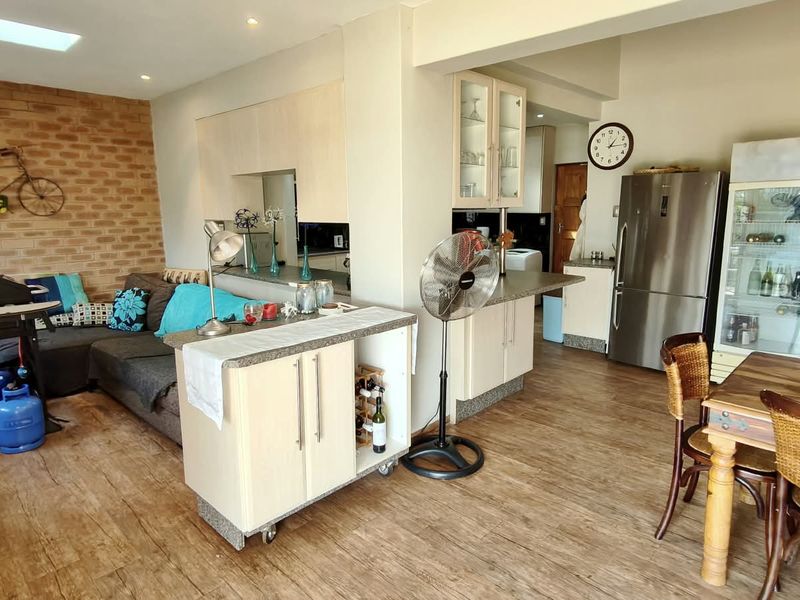 Open-plan living and kitchen area featuring laminate flooring, an exposed brick feature wall, and functional built-in cabinetry.