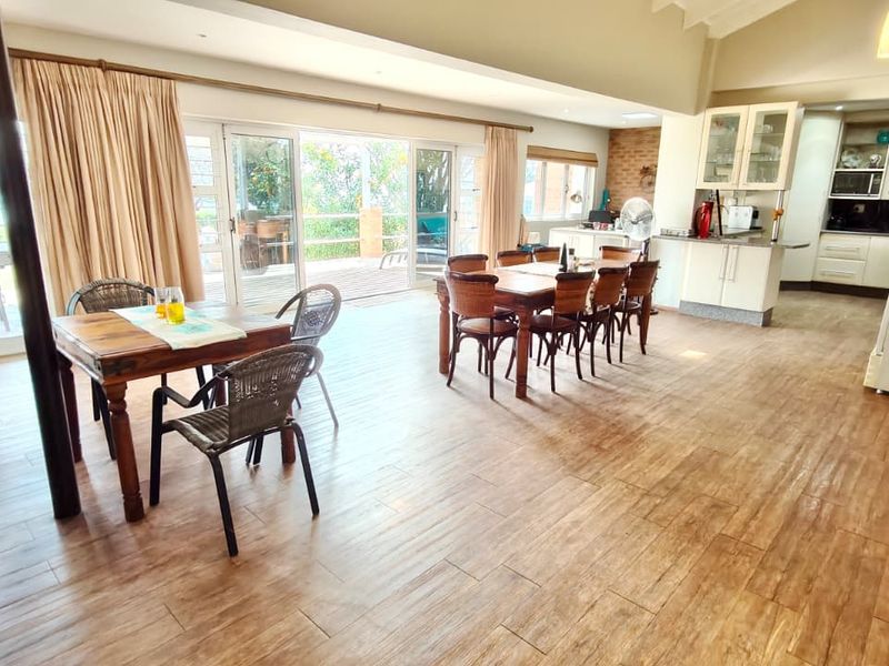 Spacious open-plan living and dining area featuring wood-look tile flooring, vaulted ceilings, and seamless access to an outdoor patio through large sliding glass doors.