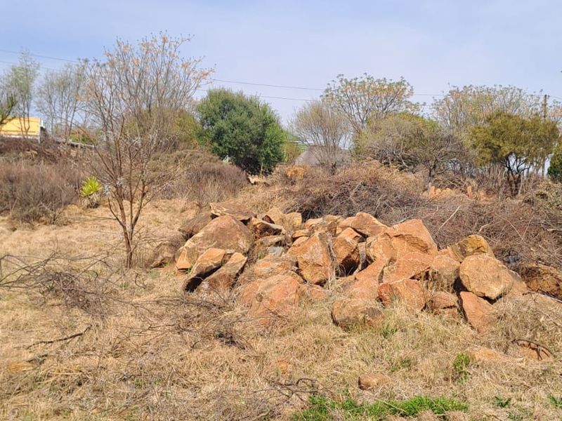 An undeveloped plot of land featuring natural rock formations and dry, overgrown vegetation.