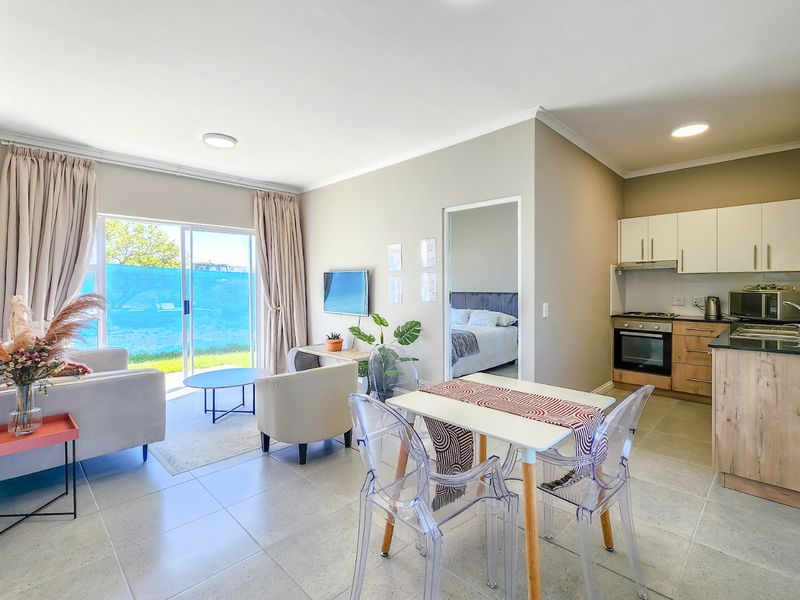 A bright open-plan living and kitchen area featuring modern cabinetry, integrated appliances, tiled floors, and a sliding door leading to an outdoor space.