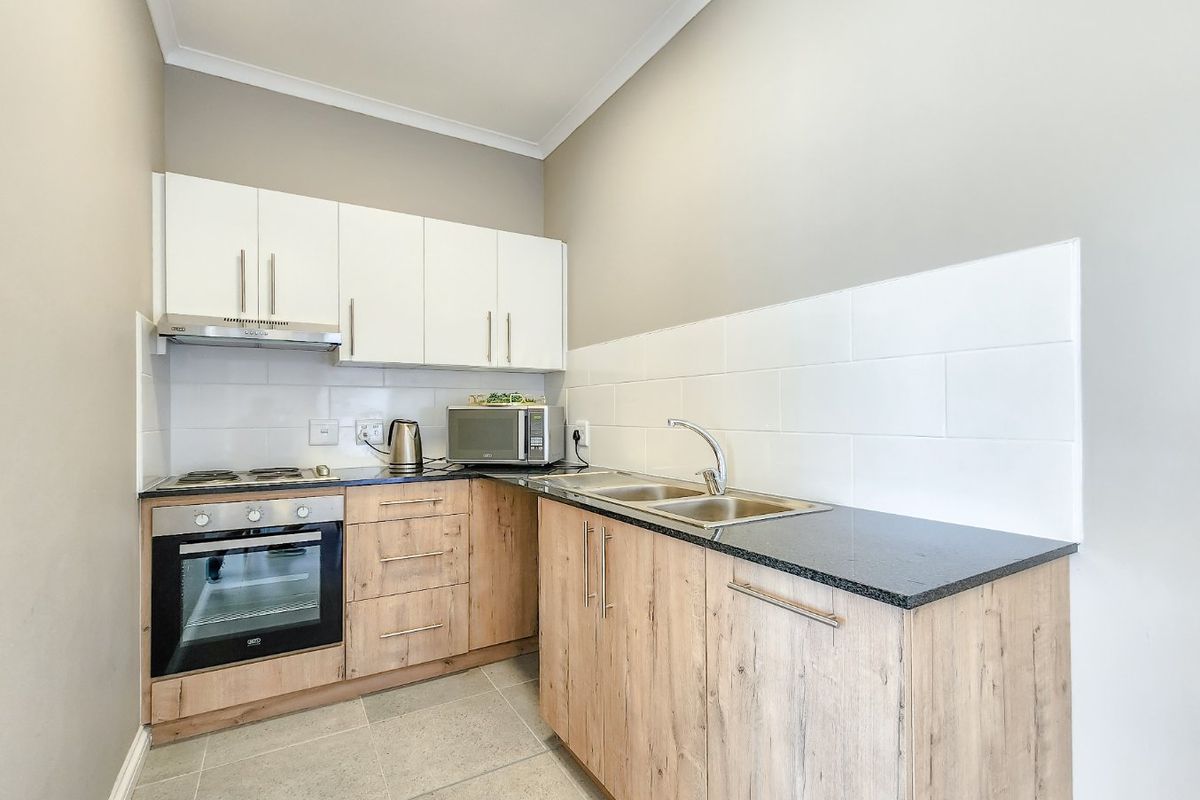 Compact modern kitchen featuring light wood-finish cabinetry, granite countertops, a double sink, built-in oven, electric hob, and a clean tiled backsplash.