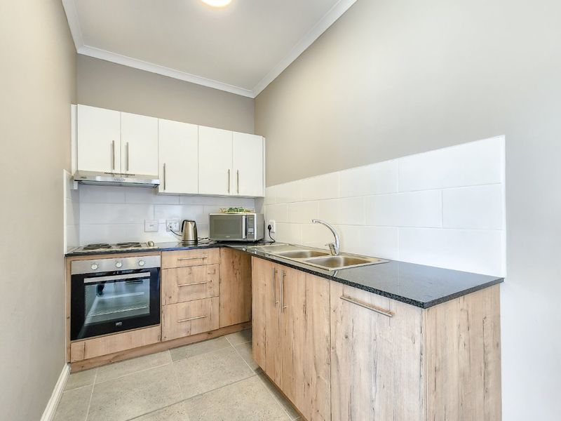 Compact modern kitchen featuring light wood-finish cabinetry, granite countertops, a double sink, built-in oven, electric hob, and a clean tiled backsplash.