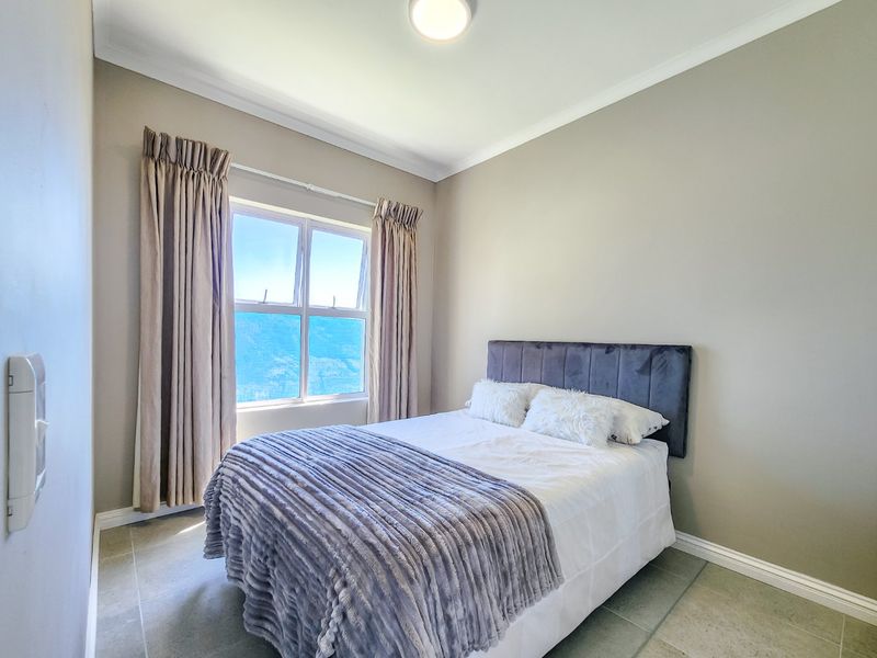 A well-maintained bedroom featuring neutral wall tones, tiled flooring, and a window with curtain tracks, offering a clean and comfortable living space.