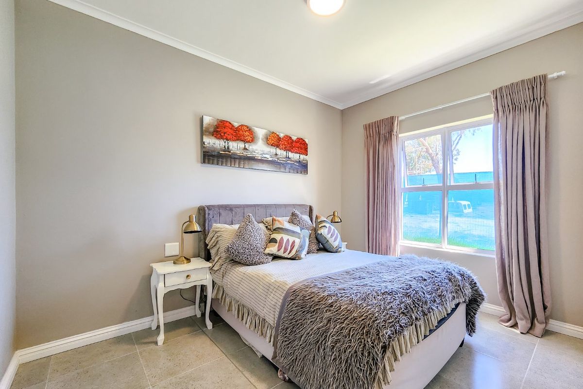 A well-maintained bedroom featuring neutral wall tones, tiled flooring, and a large window with curtain tracks.