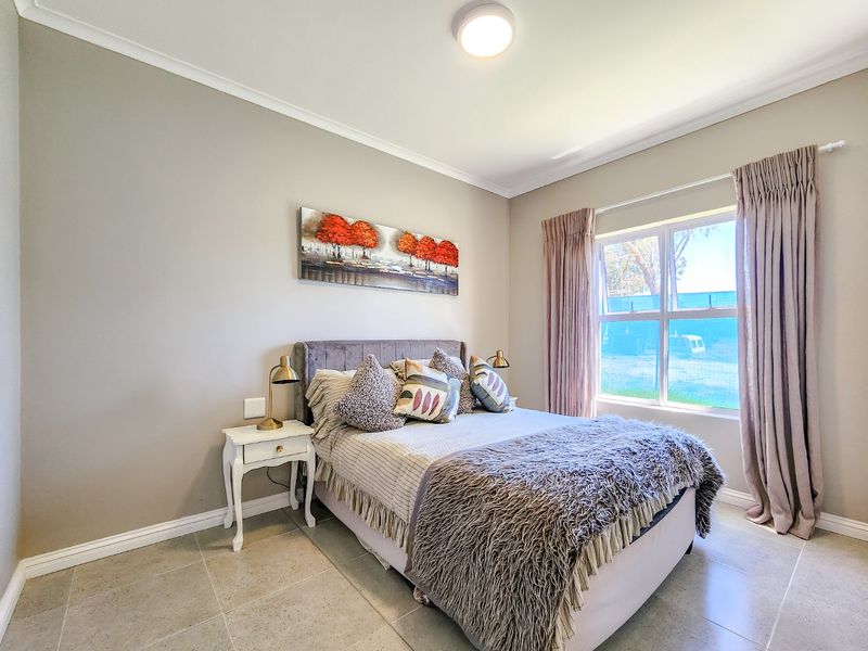 A well-maintained bedroom featuring neutral wall tones, tiled flooring, and a large window with curtain tracks.