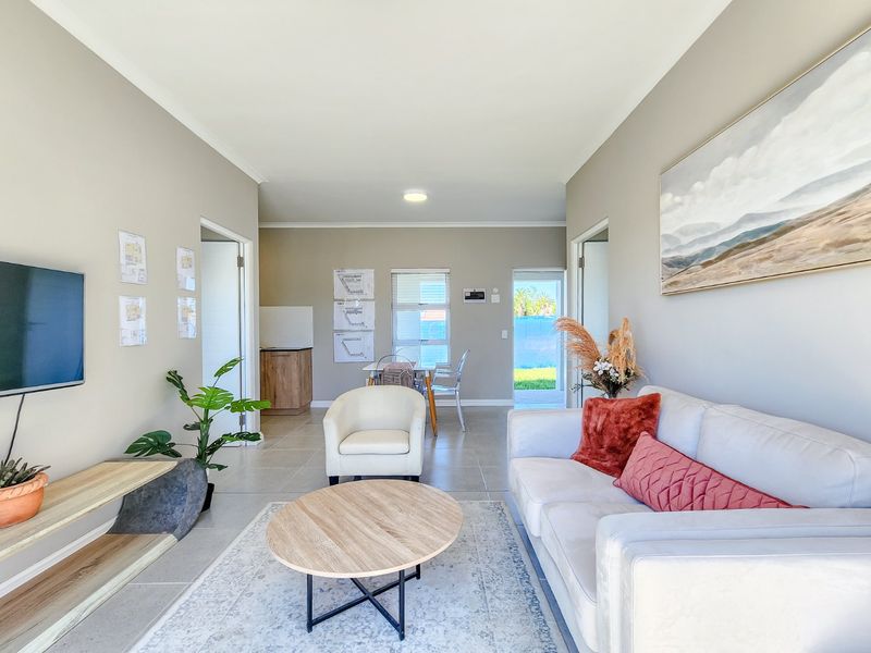 A bright open-plan living area featuring neutral wall tones, tiled flooring, and direct access to an outdoor space.