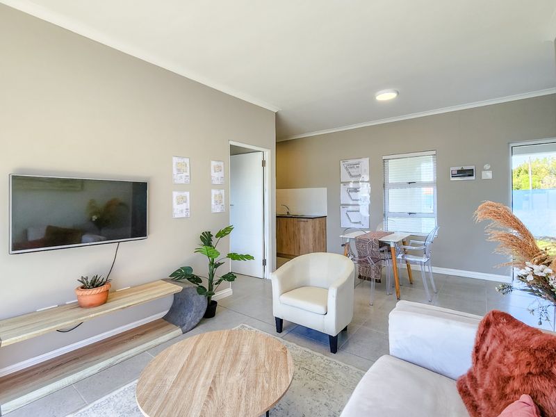 An open-plan living and kitchen area featuring neutral wall tones, tiled flooring, and a functional kitchenette with built-in cabinetry.