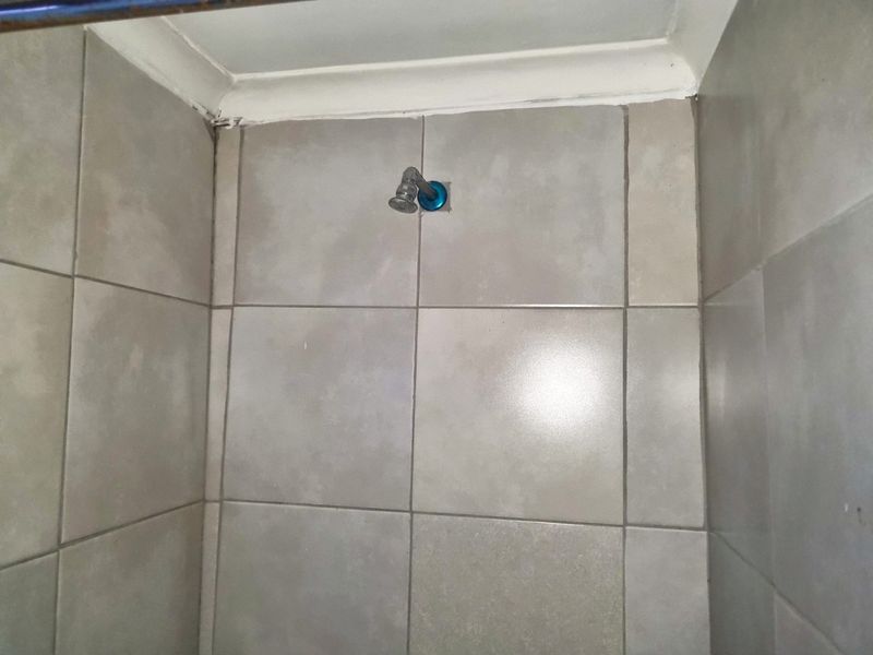 A close-up view of a shower enclosure featuring grey ceramic wall tiles and a basic shower head fixture.