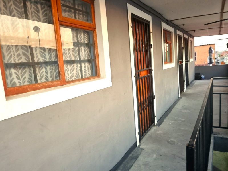 An exterior walkway or balcony area featuring security gates, timber window frames, and a metal balustrade, showing signs of wear.