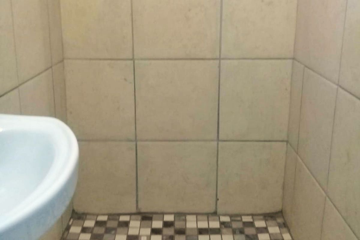 A compact shower enclosure featuring mosaic floor tiling and neutral wall tiles, accompanied by a pedestal basin.
