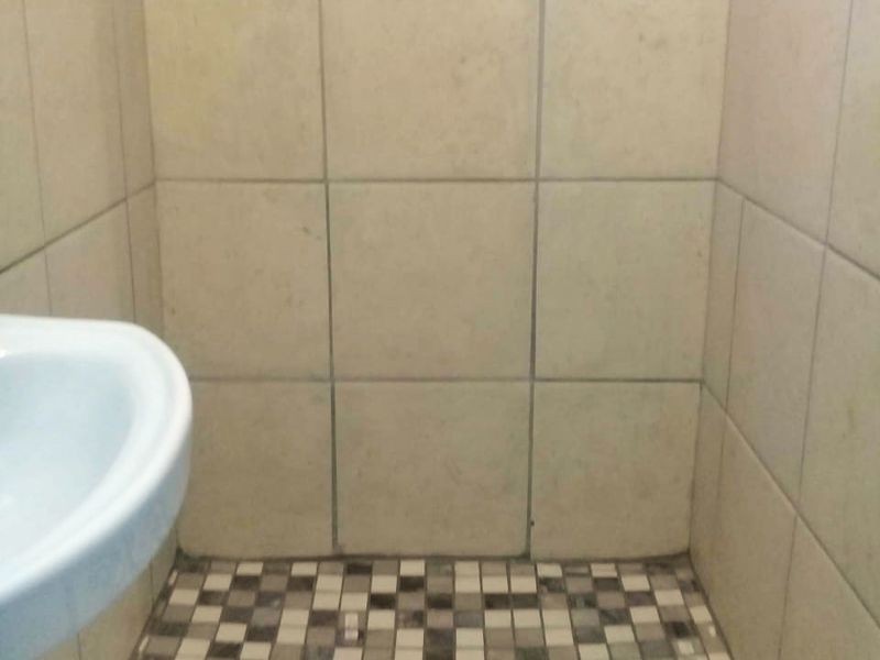 A compact shower enclosure featuring mosaic floor tiling and neutral wall tiles, accompanied by a pedestal basin.