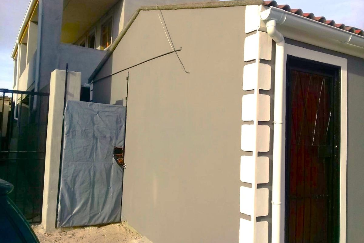 Rear exterior view of the property featuring painted masonry walls, decorative quoins, and a security gate entrance.