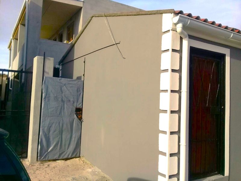 Rear exterior view of the property featuring painted masonry walls, decorative quoins, and a security gate entrance.