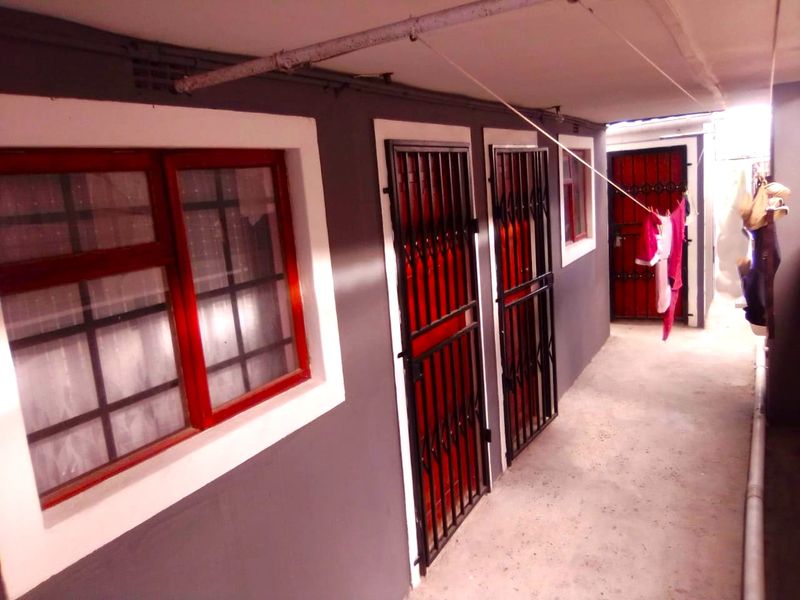 An exterior covered walkway featuring concrete flooring, security gates, and window frames, providing access to multiple entry points.