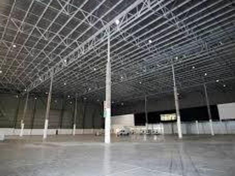 Spacious industrial warehouse interior featuring high ceilings with exposed steel trusses, concrete flooring, and structural support columns.