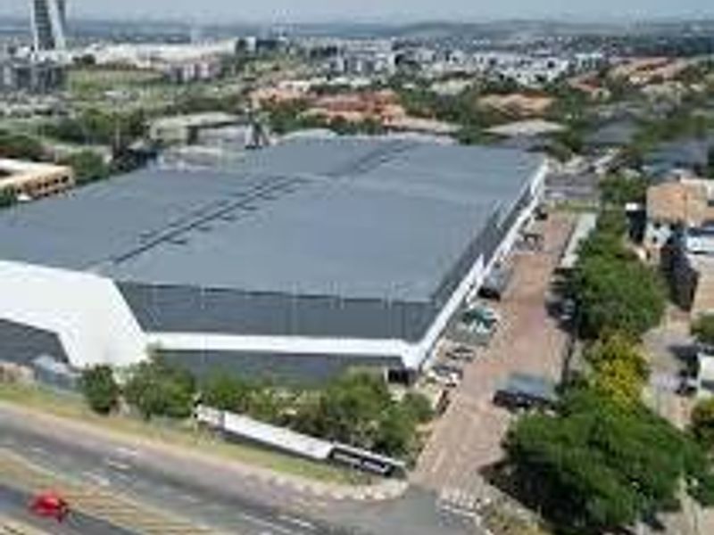 Aerial view of a large industrial warehouse facility featuring a metal roof, paved driveway, and perimeter fencing in a commercial business park setting.