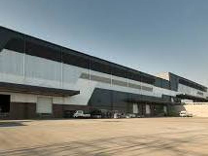 Modern industrial warehouse facility featuring extensive loading docks, roller shutter doors, and a spacious concrete yard for logistics operations.