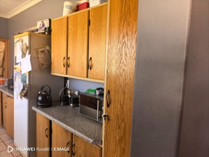 A functional kitchen area featuring traditional wooden cabinetry, laminate countertops, and a tall built-in pantry cupboard, offering potential for modern cosmetic updates.