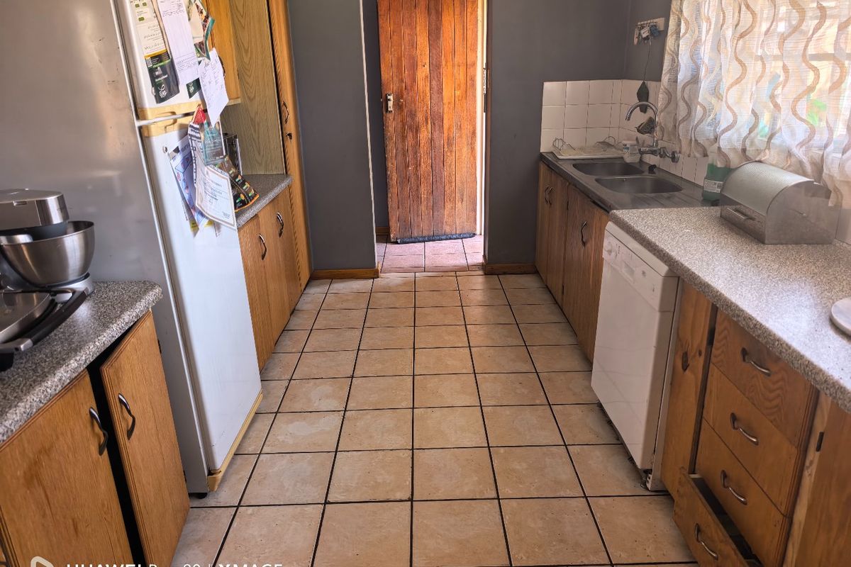 A functional kitchen featuring wooden cabinetry, laminate countertops, and tiled flooring, offering a dated aesthetic with potential for modern renovation.