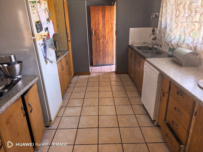 A functional kitchen featuring wooden cabinetry, laminate countertops, and tiled flooring, offering a dated aesthetic with potential for modern renovation.