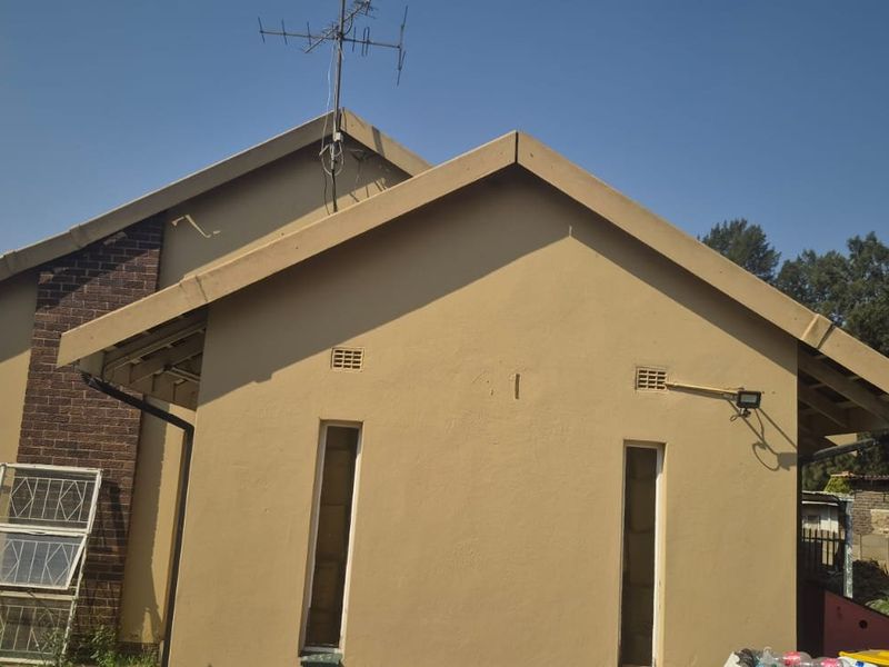 Rear view of the house featuring a pitched roof, brick chimney, and exterior security lighting, showing standard maintenance requirements.