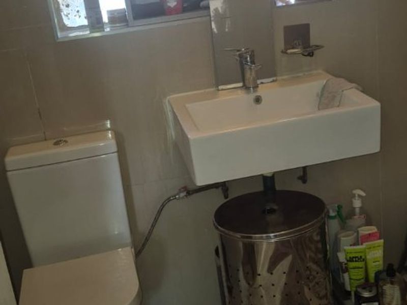 A compact bathroom featuring a wall-mounted basin, toilet, and tiled finishes. The space includes a window with security bars.