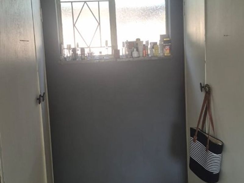 A narrow hallway featuring built-in storage cupboards, tiled flooring, and a window with security bars.
