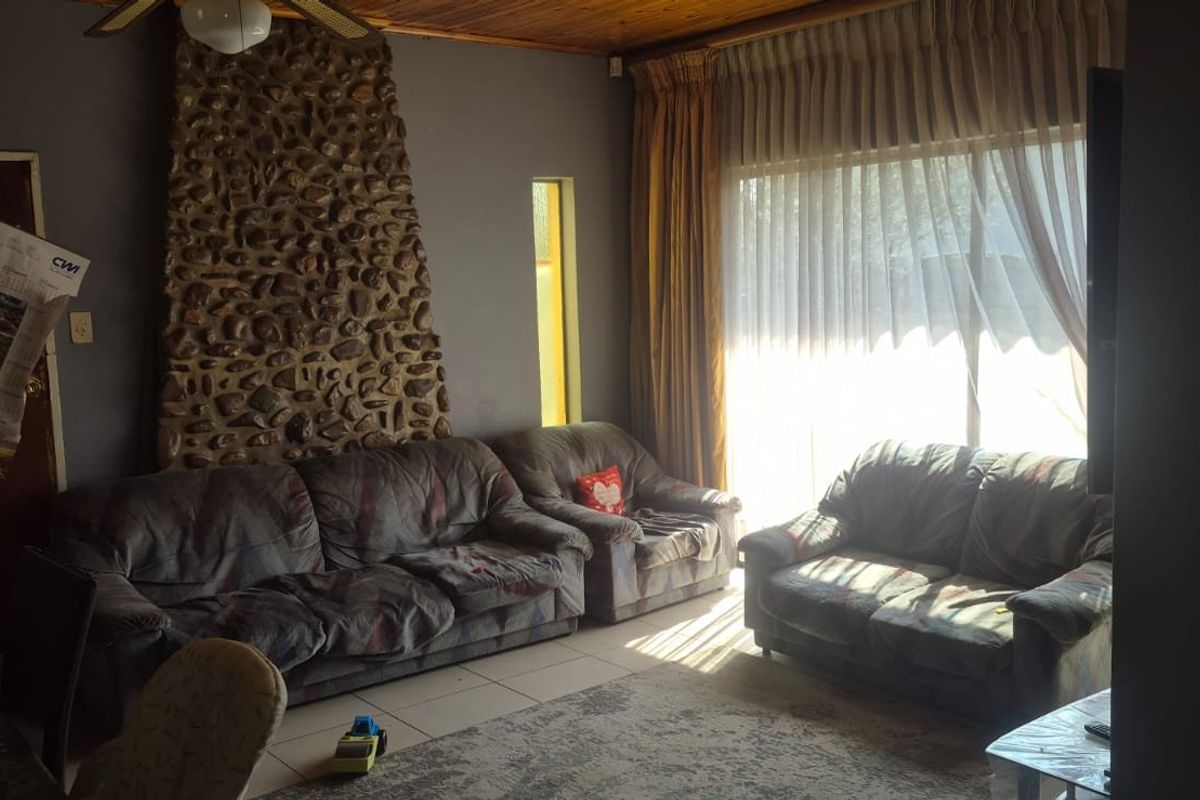 Living room featuring a prominent stone fireplace, timber ceiling, and large sliding glass doors providing natural light.