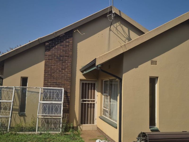 Rear elevation of a single-story house featuring a brick chimney, security gate, and painted exterior walls.