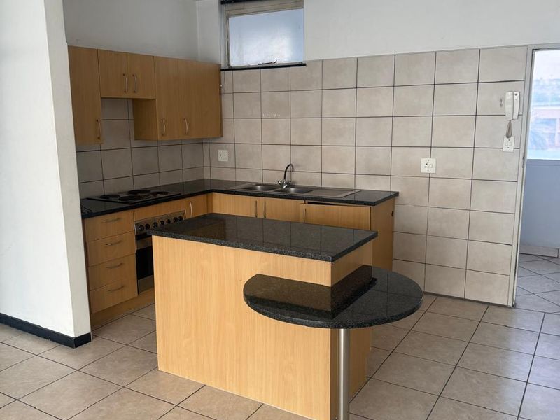 Functional kitchen featuring laminate cabinetry, granite countertops, built-in oven, electric hob, and a breakfast nook, finished with neutral ceramic wall and floor tiles.