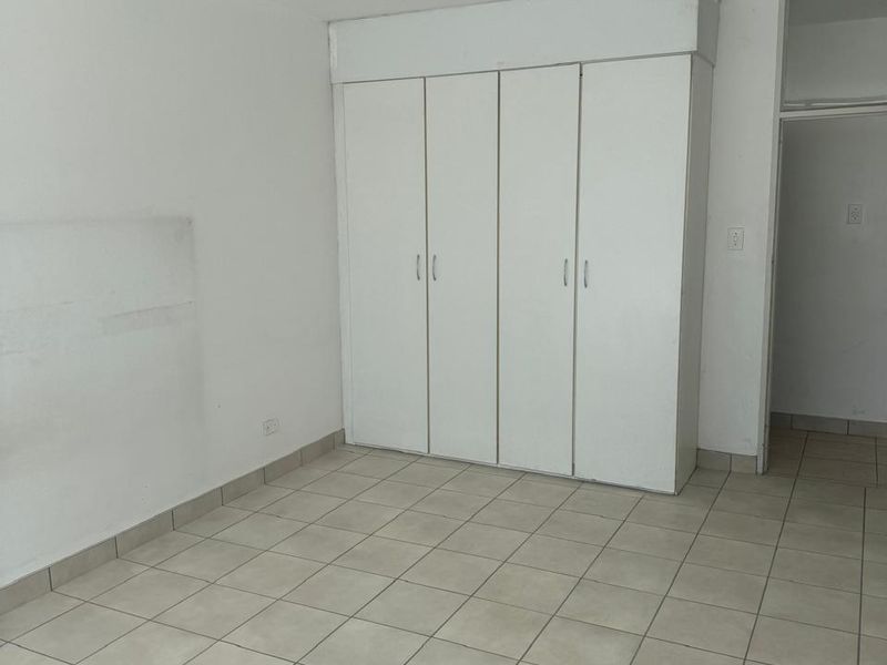 An empty bedroom featuring ceramic tile flooring, a built-in wardrobe, and a ceiling spotlight fixture, ready for personalization.