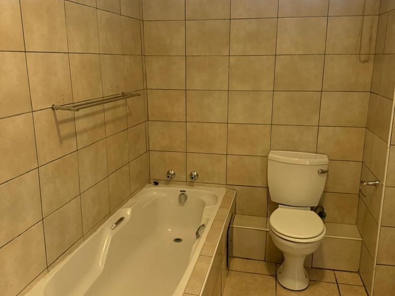 A functional bathroom featuring a built-in bathtub, toilet, and neutral ceramic tiling throughout, offering a clean and practical space.