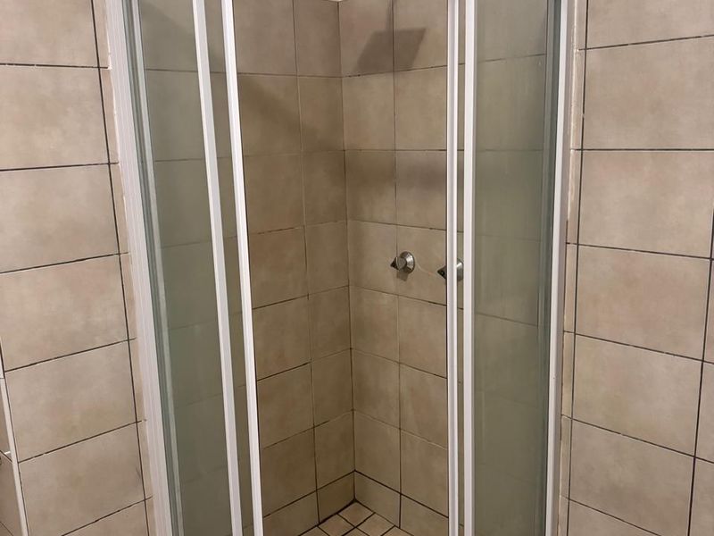 A corner shower unit featuring a glass enclosure, modern shower head, and neutral wall and floor tiling.