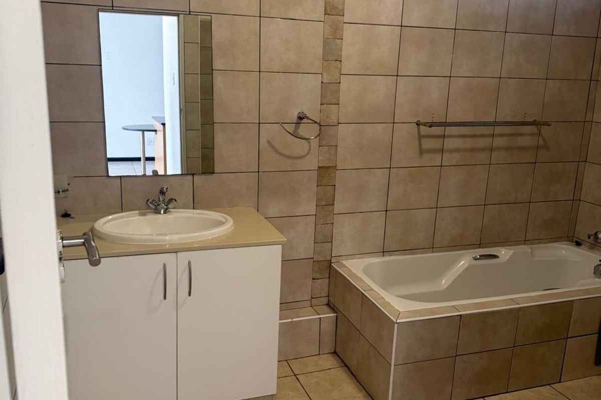 A functional bathroom featuring a tiled bathtub, vanity cabinet with basin, and neutral ceramic wall and floor tiling.