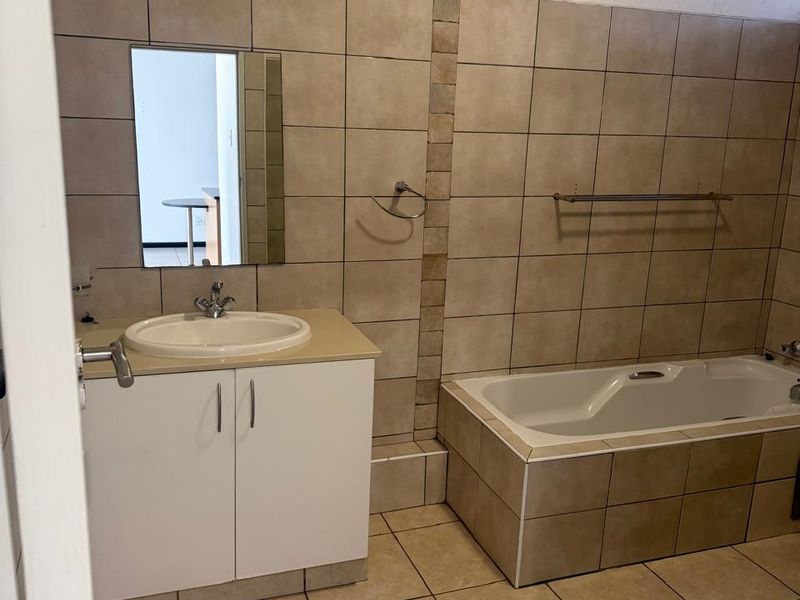 A functional bathroom featuring a tiled bathtub, vanity cabinet with basin, and neutral ceramic wall and floor tiling.