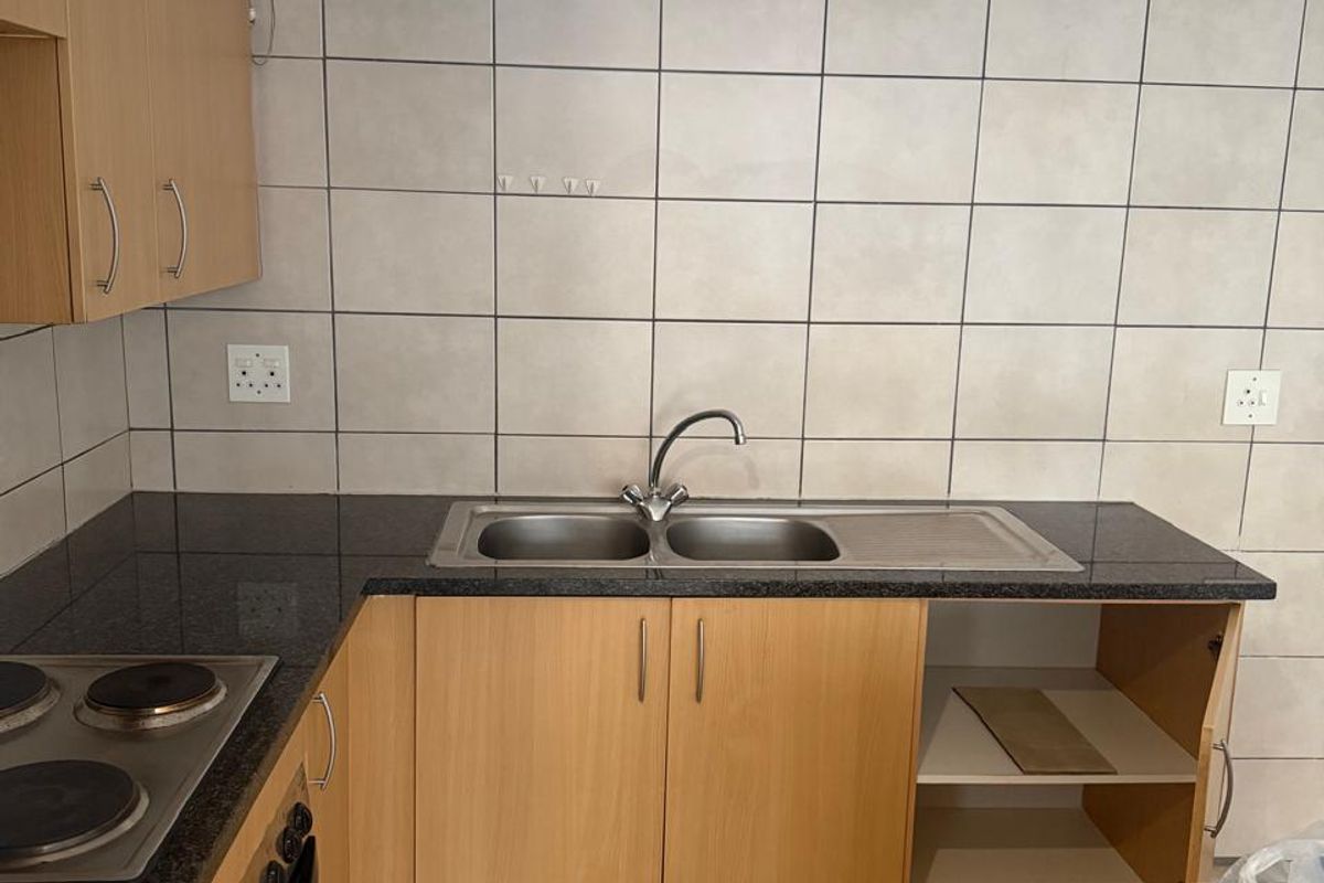 A functional kitchen featuring laminate cabinetry, granite countertops, a built-in oven and hob, and tiled finishes throughout.
