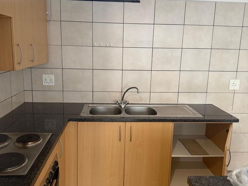 A functional kitchen featuring laminate cabinetry, granite countertops, a built-in oven and hob, and tiled finishes throughout.