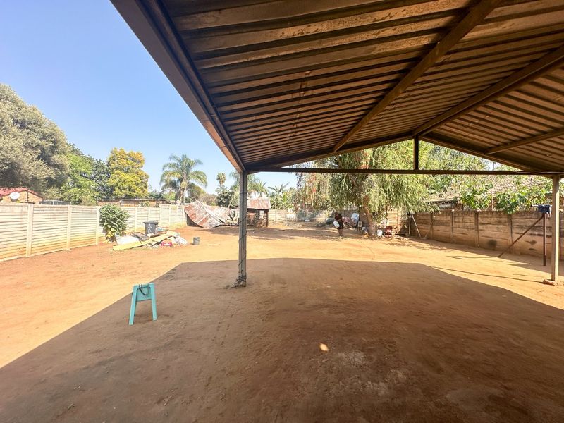 A large covered outdoor patio area featuring a metal roof structure and open access to a spacious, unpaved backyard with perimeter walling.