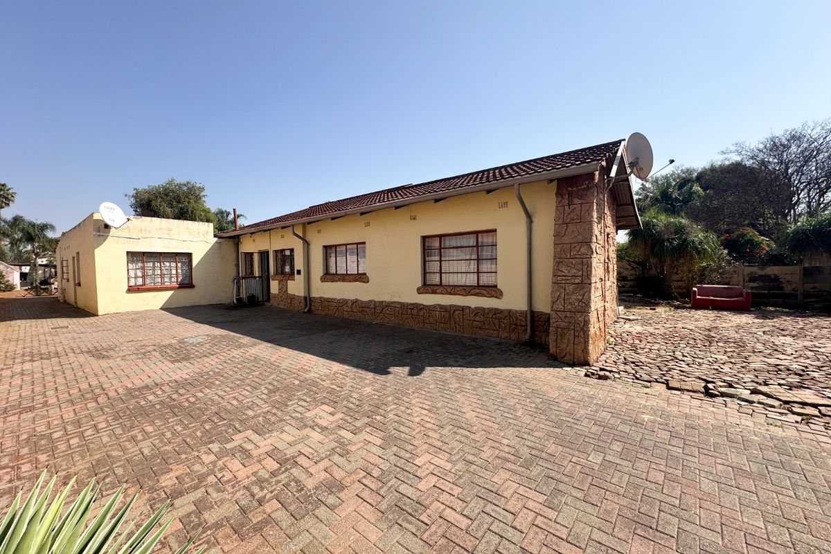 Rear exterior view of the property featuring a large paved courtyard, stone-clad corner detailing, and a tiled roof structure.