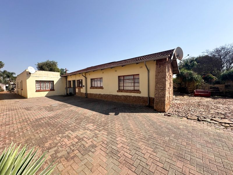 Rear exterior view of the property featuring a large paved courtyard, stone-clad corner detailing, and a tiled roof structure.