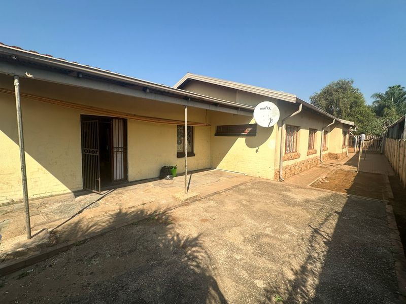 Rear exterior view of the house featuring a covered patio area, paved ground, and security gate access.