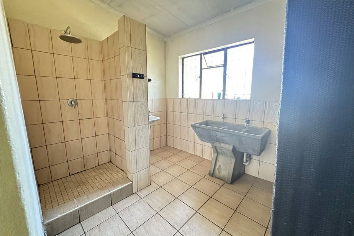 A functional bathroom featuring a tiled shower enclosure, concrete double sink, and tiled flooring, offering potential for modernization and cosmetic updates.